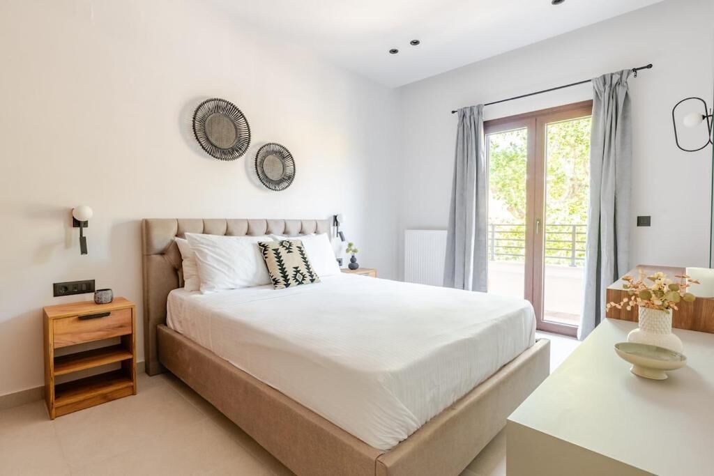 A bedroom with a bed, bedside tables, a nightstand, a window with curtains, and wall decor.