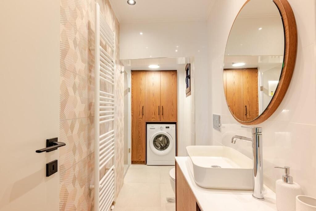 Une salle de bain moderne avec un lave-linge intégré, un grand miroir et un lavabo blanc.