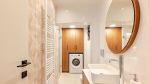 A modern bathroom with a built-in washing machine, a large mirror, and a white sink. - Spacious Luxury apt , old Town (Chania)