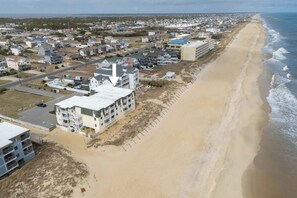 A coastal town with a beachfront hotel featuring multiple floors, a parking area, and a sandy beach. - Beachfront Condo with Ocean Views and Pool Access! (Kill Devil Hills)