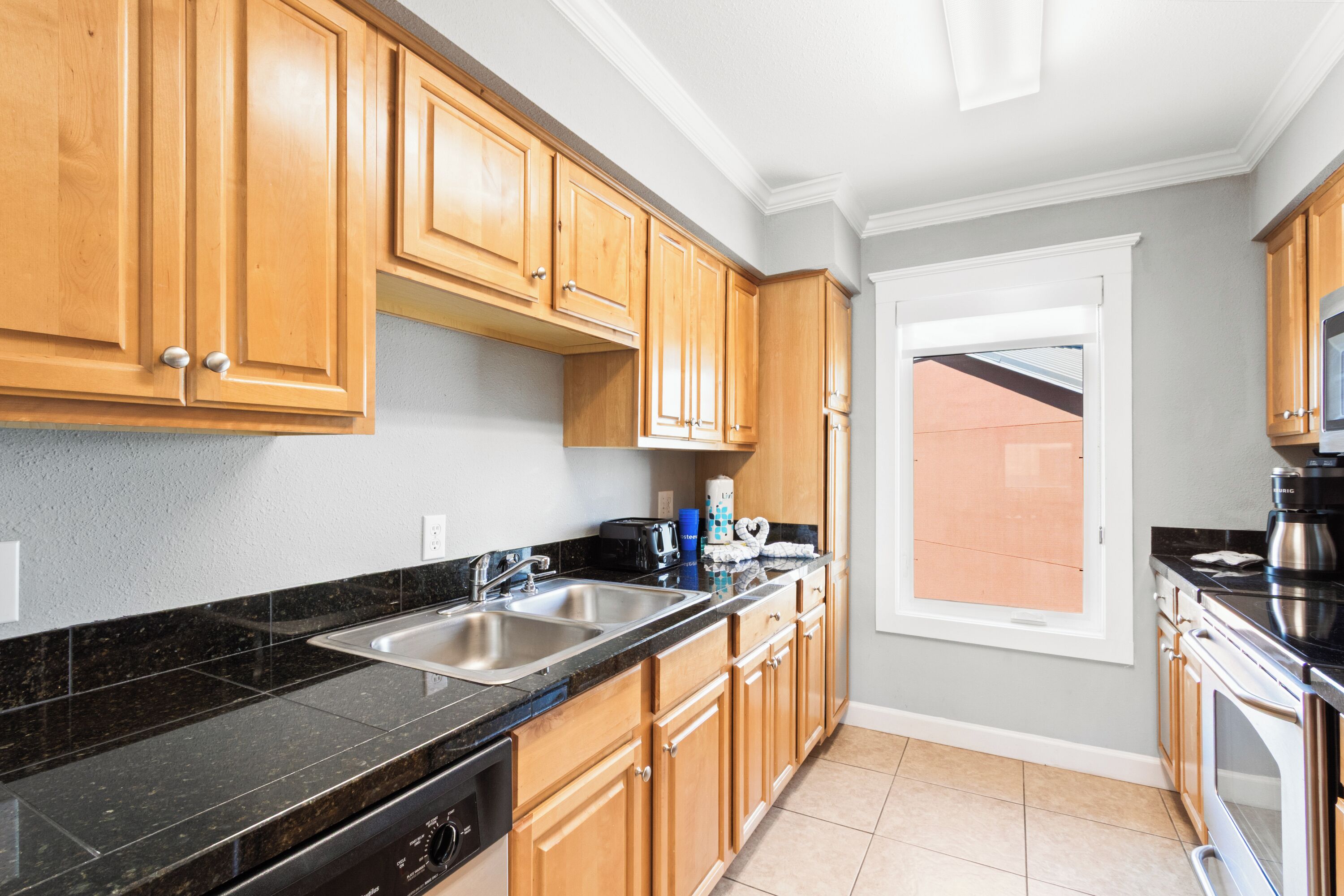A kitchen with wooden cabinets, black countertops, stainless steel appliances, and a window with a view.