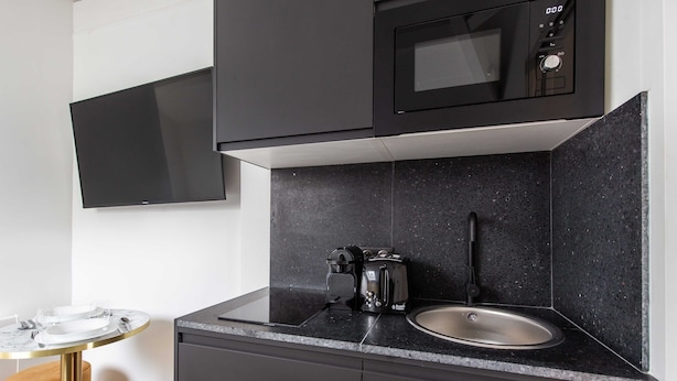 A modern kitchen with a black microwave, a sink, and a coffee maker on the countertop. - Cosy Studio - 2P - Parc des Expositions (Paris)