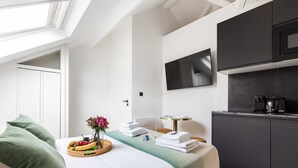 A modern hotel room with a bed, a small kitchenette, a flat-screen TV, and a skylight. - Cosy Studio - 2P - Parc des Expositions (Paris)