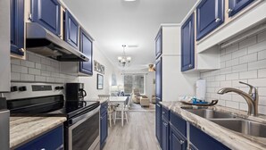 A kitchen with dark blue cabinets, a white tiled backsplash, stainless steel appliances, and a marble countertop.