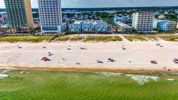 A beach with several buildings in the background, including a tall hotel and a smaller structure with a blue roof.