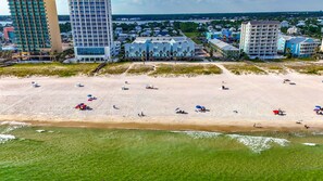 A beach with several buildings in the background, including a tall hotel and a smaller structure with a blue roof.
