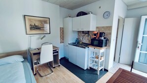 A compact hotel room with a bed, a desk with a chair, a kitchenette with a microwave, and a small window. - Cozy apartment for single person in 5 minutes from Friedrichsdorf train station (Friedrichsdorf)