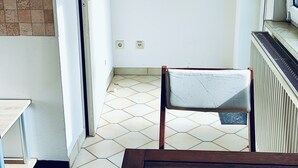A room with a wooden bench, a white door, a tiled floor, a radiator, and a wall-mounted clock. - Cozy apartment for single person in 5 minutes from Friedrichsdorf train station (Friedrichsdorf)