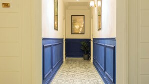 En hall med ett mönstrat golv, blå paneler längs väggarna, en kristallkrona och inramade konstverk på väggarna.