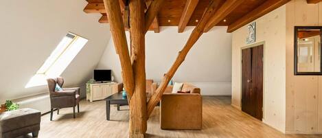 A loft-style room with exposed wooden beams, a television, seating area, and a large window.
