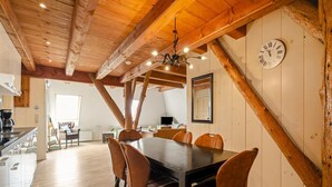 Un espace repas avec un plafond en bois, une grande horloge et une vue sur une autre pièce.