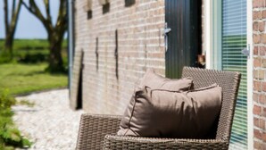 Une chaise en osier avec un coussin, placée à l’extérieur d’un bâtiment en briques doté d’une fenêtre.
