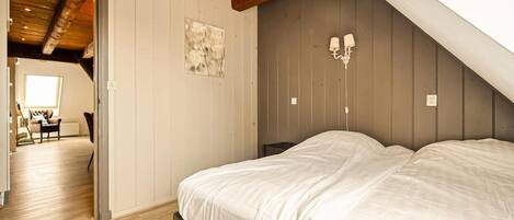 Quarto com teto inclinado, uma cama, luminária fixada na parede e uma janela.
