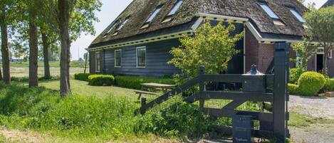 A traditional thatched-roof house with a wooden gate and a picnic table in front.