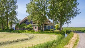 Une maison de campagne avec un toit de chaume, entourée d’une végétation luxuriante et bordée d’un chemin étroit.