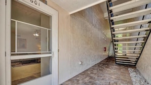 Un pasillo con suelo de baldosas, una puerta con ventana de malla y una escalera con barandillas de metal.