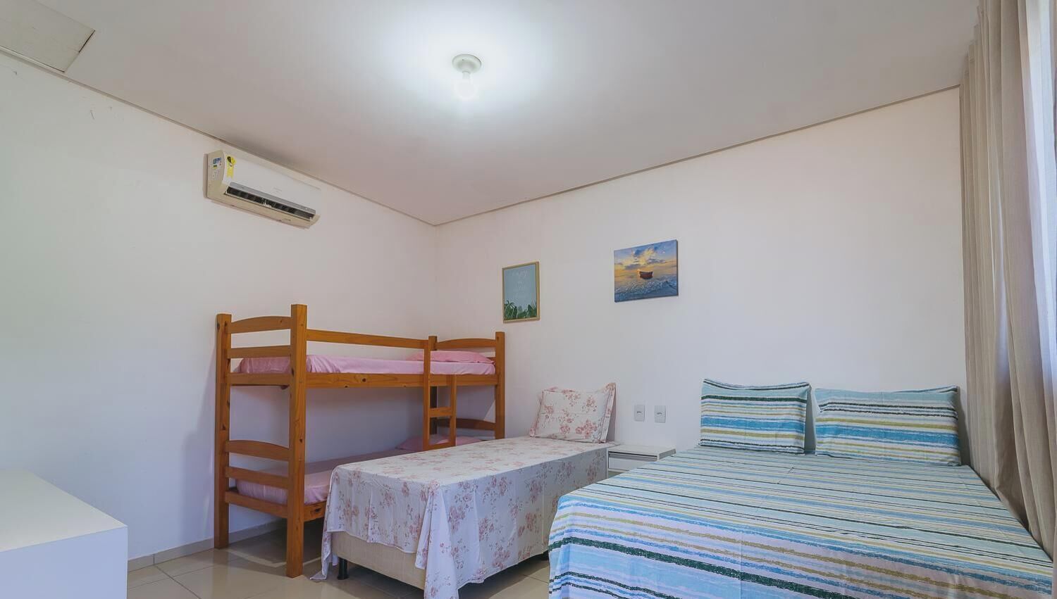 A room with bunk beds, a single bed, a small table, and a painting on the wall.