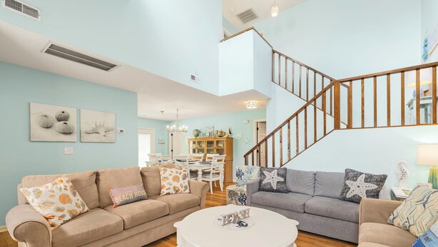 A spacious living room with a beige sofa, a gray sofa, and a white coffee table. A wooden staircase with a railing leads to an upper level.