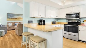 A modern kitchen with white cabinets, a granite countertop, a built-in oven, and a microwave. There are two stools in front of the kitchen island.