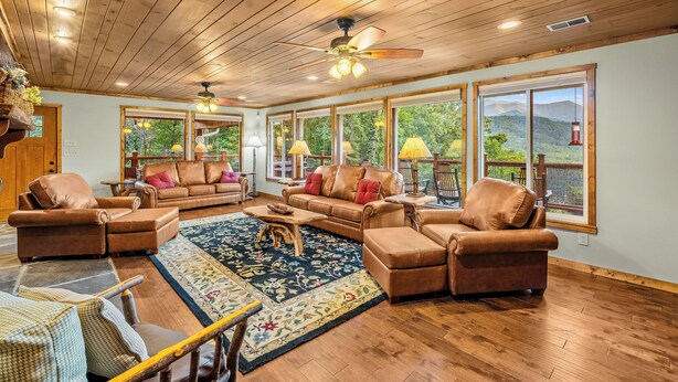 A spacious living room with wooden flooring, leather sofas, and large windows offering a view of the outdoors. - Hesed Retreat | Views + Secluded + Hot Tub (Gatlinburg)