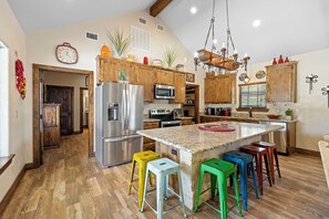 A spacious kitchen with wooden cabinets, stainless steel appliances, and a central island with colorful stools.