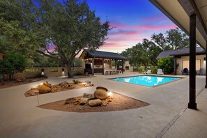 A backyard with a swimming pool, a barbecue area, and a covered patio.