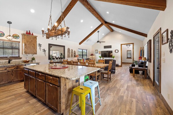 A spacious kitchen with a large island, wooden cabinets, and a high ceiling with exposed beams.
