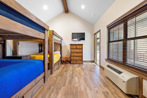 A room with bunk beds, a television, a heater, and a window with blinds. - El Ranchito (Golf Included through May 2027): 4 BR, 4.5 BA House in Concan, Sleeps 20 (Concan)