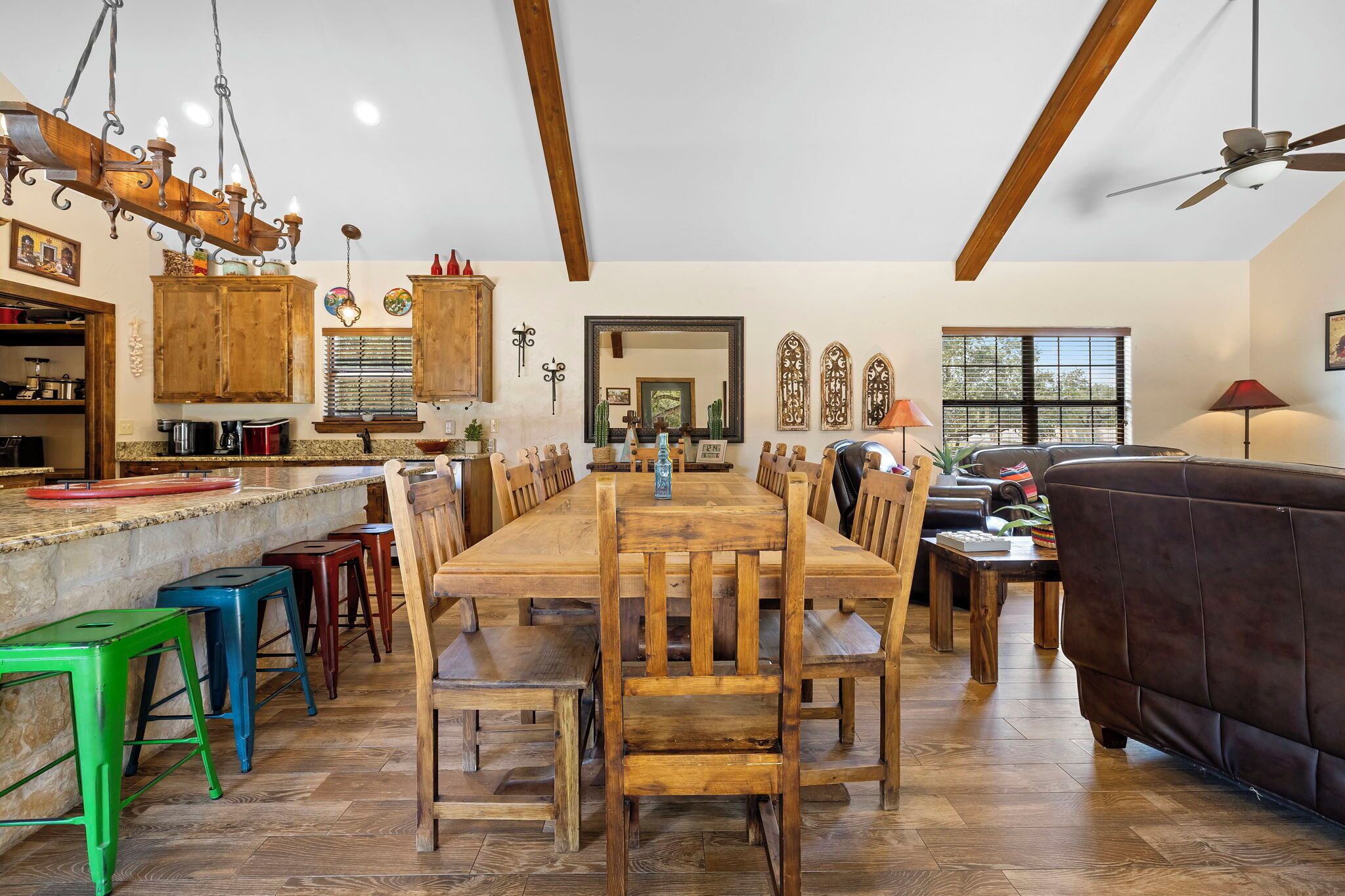 A spacious dining area with a long wooden table and matching chairs, a kitchen with wooden cabinets, and a ceiling fan.