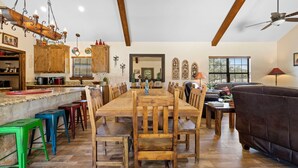 A spacious dining area with a long wooden table and matching chairs, a kitchen with wooden cabinets, and a ceiling fan. - El Ranchito (Golf Included through May 2027): 4  BR, 4.5  BA House in Concan, Sleeps 20 (Concan)