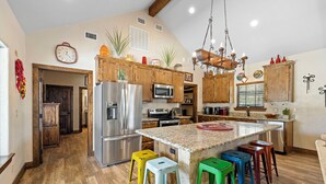 A spacious kitchen with wooden cabinets, stainless steel appliances, and a central island with colorful stools. - El Ranchito (Golf Included through May 2027): 4  BR, 4.5  BA House in Concan, Sleeps 20 (Concan)