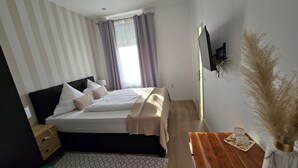 A hotel room with a bed, a desk with a vase, and a TV on the wall. - Hotel Kronprinz  (Emden)