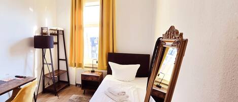 A hotel room with a bed, a desk, a chair, and a mirror.
