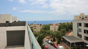 Une vue d’une zone côtière avec des bâtiments, une route où sont garées des voitures et un ciel dégagé.