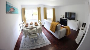 Un coin repas avec une table dressée pour quatre personnes, un canapé blanc, un téléviseur et un meuble.