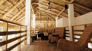 A wooden deck with a thatched roof, a sofa, and a woven chair.