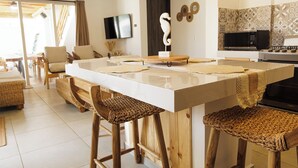 A modern kitchen with a white countertop, wooden stools, and a TV mounted on the wall.