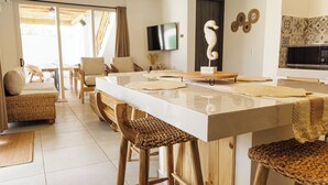 A modern kitchen with a large island, wooden stools, and a television mounted on the wall.