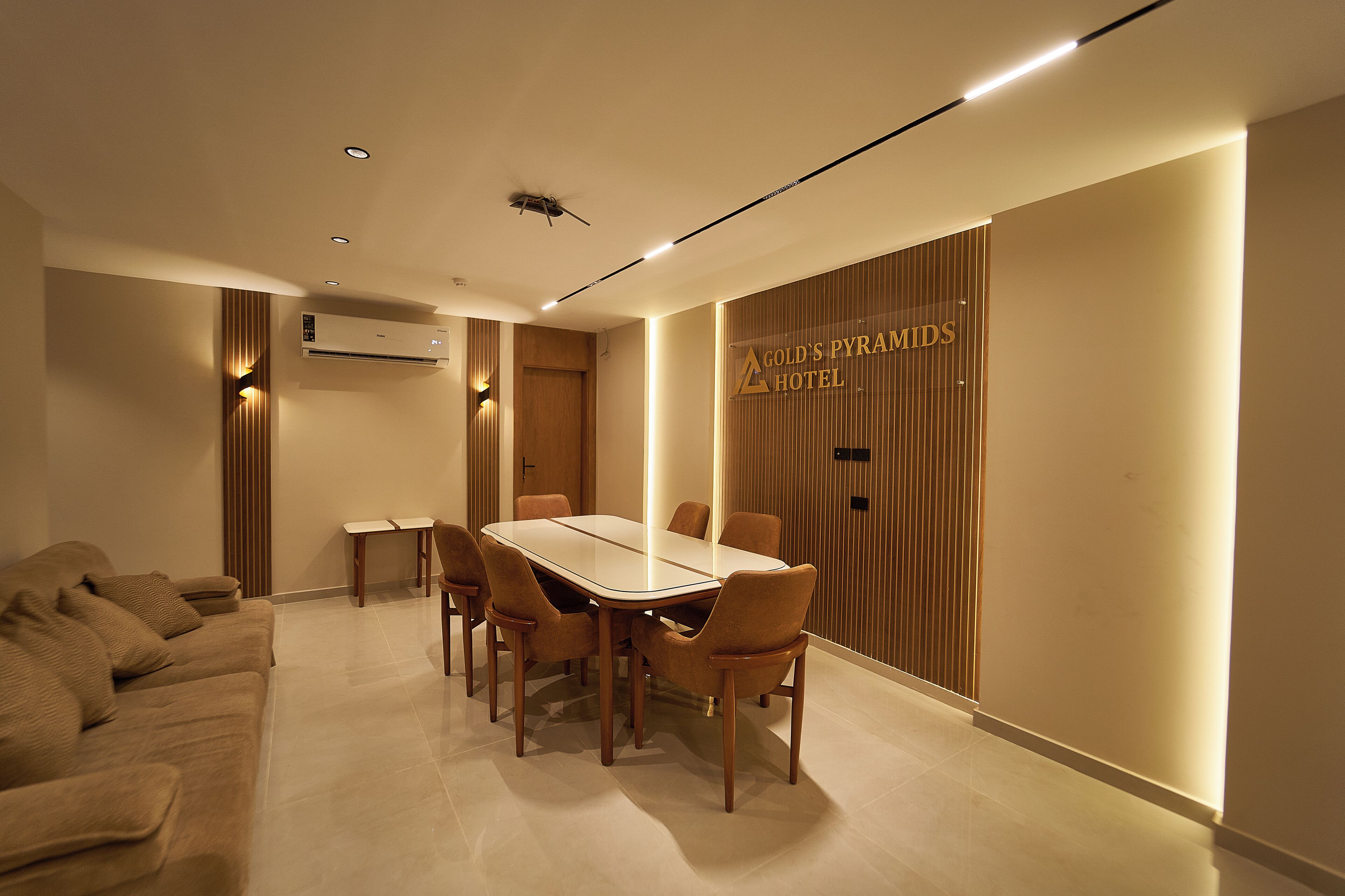 A modern hotel room with a dining area, a sofa, and a wall-mounted air conditioning unit.
