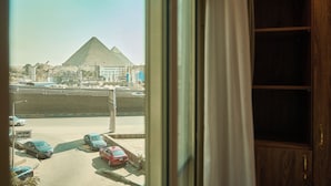 A view of a pyramid through a window, with a parking lot and buildings in the foreground. - New Gold's Pyramids Hotel (Giza)
