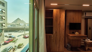 A modern hotel room with a large window, a desk, a television, and a wardrobe. - New Gold's Pyramids Hotel (Giza)