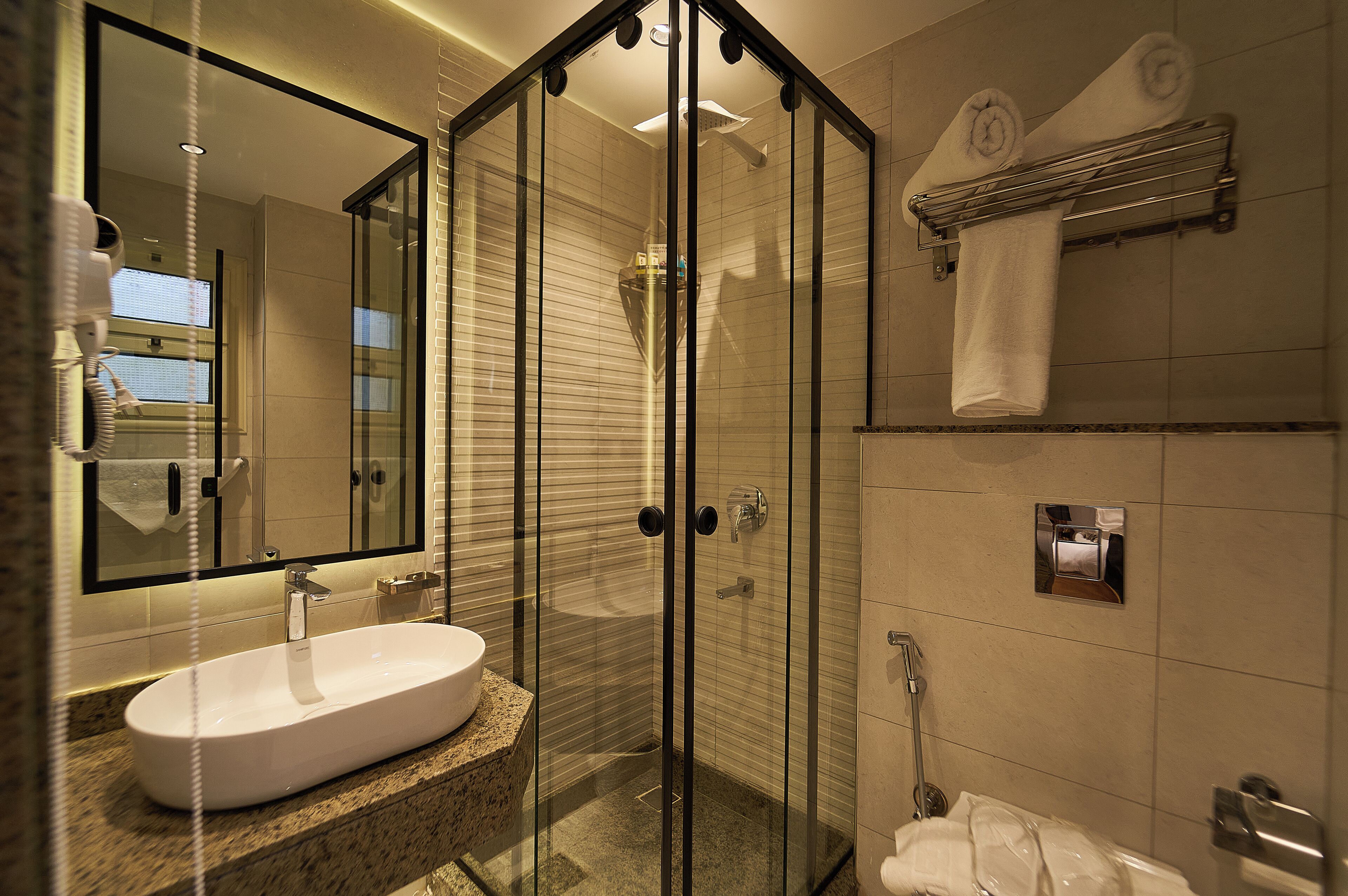 A modern bathroom with a glass-enclosed shower, a white sink, and a towel rack.