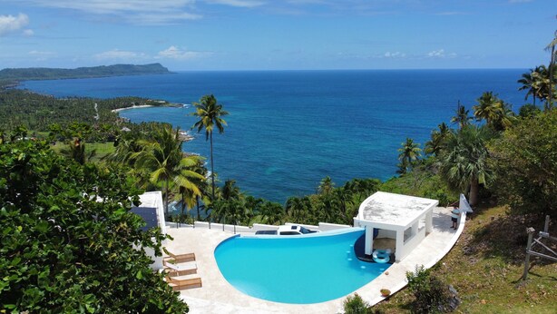 A pool with a view of the ocean, surrounded by palm trees and a white building. - Mountaintop villa for film, TV and photo shoots only.  Not for vacation rental. (Samana)