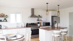 Une cuisine moderne dotée d’un îlot central, d’appareils électroménagers en acier inoxydable et de luminaires suspendus.