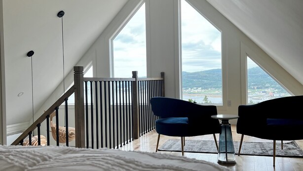 Une chambre avec un grand lit, une vue sur l’extérieur par une fenêtre et un balcon avec une balustrade.