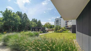 A modern building with a paved pathway, lush greenery, and a clear sky.