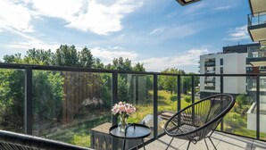 A balcony with a glass railing, a small table with a vase of flowers, and a black chair.