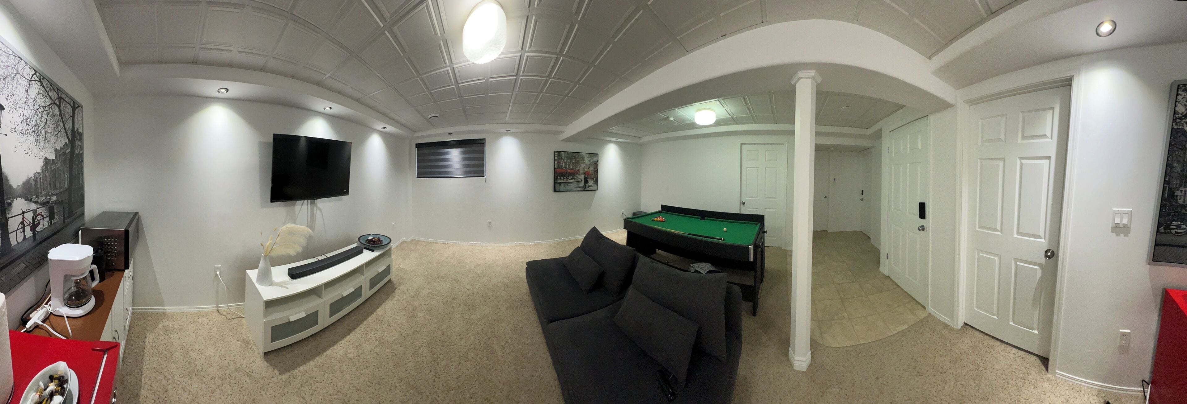 Un vaste salon comprenant une table de billard, un téléviseur à écran plat fixé au mur et un coin salon confortable avec un canapé.