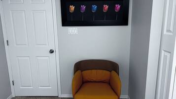 A room with a white door, a framed picture of flowers on the wall, and a mustard-colored chair.