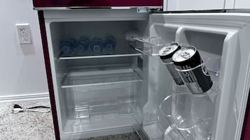 Ein offener Kühlschrank mit klaren Regalen, ein paar Wasserflaschen und zwei Dosen Limonade.